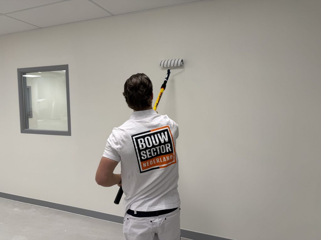 Schilder rolt een gebroken witte muur naast een binnenraam met grijs kozijn