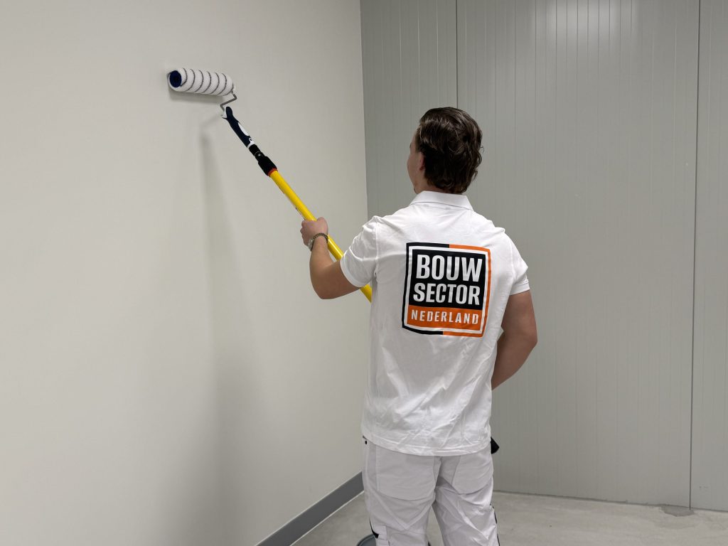 Schilder met gele verlengsteel zet een verfroller op een witte wand