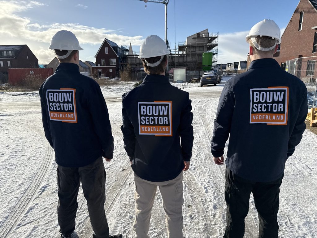 Drie vakmensen van Bouwsector Nederland met bouwhelm op de rug gezien bij een nieuwbouwwijk in de sneeuw